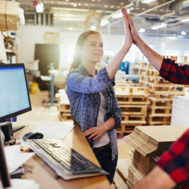Two Caucasian coworkers congratulating each other while working in a warehouse